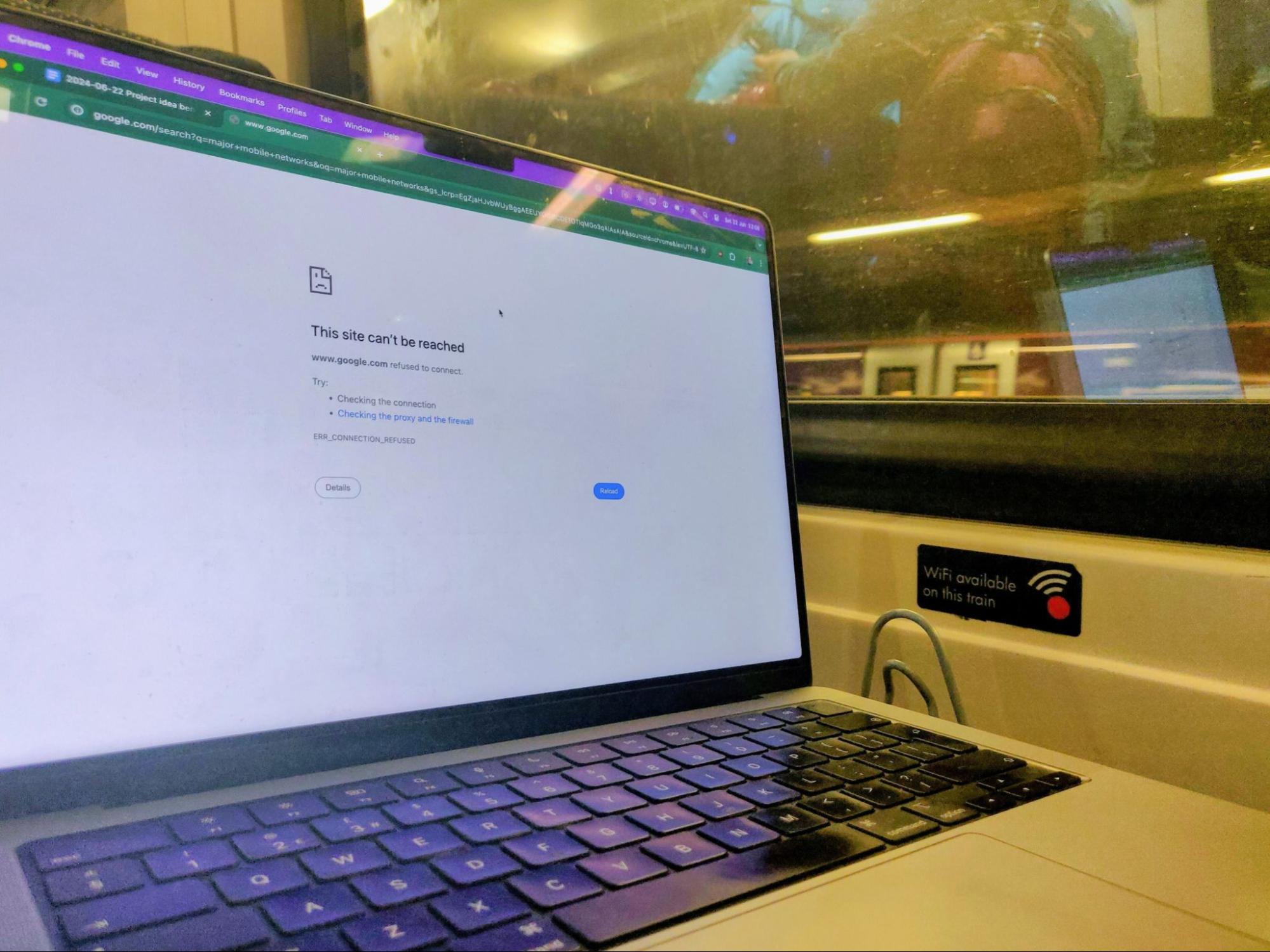 Laptop in a train displaying 'This site can't be reached', next to a sticker saying 'WiFi available on this train'